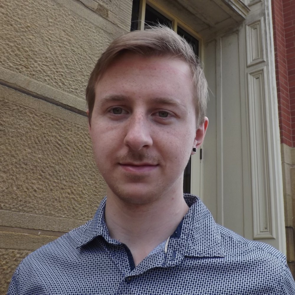 Portrait of Hunter Tenney outdoors in front of a sandstone and brick building.