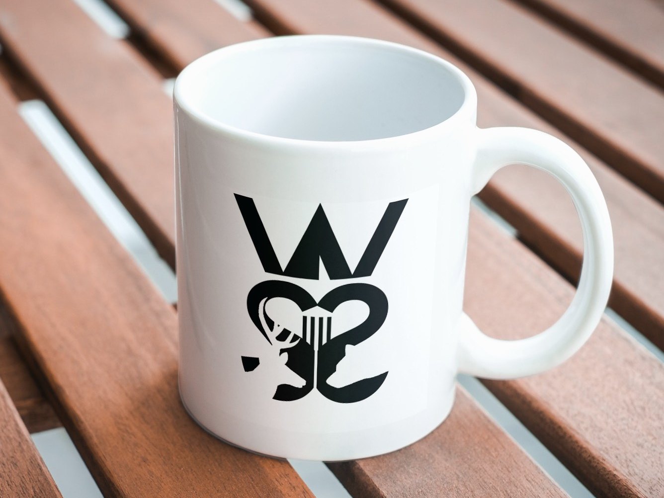 The final White Sulphur Springs logo printed in black on a white mug: a bold W above two mirrored S shapes that form a heart, with a deer and the columns of the town's main building set inside.